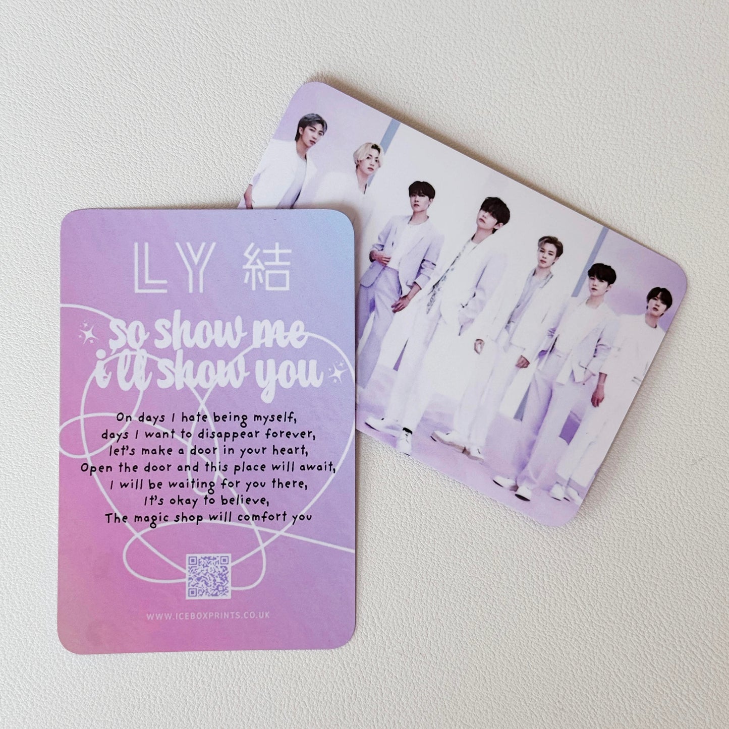 Two rectangular printed cards or photocards on a light background. The front card is lavender with white text reading 'LY 結 so show me i'll show you' and a song lyric, while the back card shows a group photo of seven young men in white outfits.