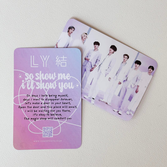 Two rectangular printed cards or photocards on a light background. The front card is lavender with white text reading 'LY 結 so show me i'll show you' and a song lyric, while the back card shows a group photo of seven young men in white outfits.